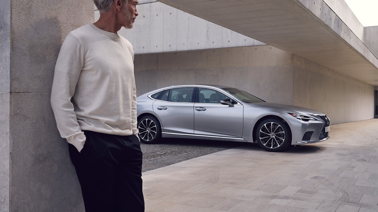A man stood in the foreground of a parked Lexus LS 
